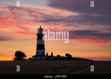 Happisburgh Leuchtturm an der Ostküste von England umgeben von Ein Weizenfeld mit einem atemberaubenden Sonnenuntergang in der Hintergrund Stockfoto