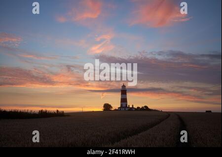 Dramatische Sonnenuntergangsfarbe am Himmel an der Norfolk-Küste In Happisburgh mit dem ikonischen Leuchtturm in der Ferne Stockfoto