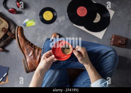 Männliche Hand hält Tasse Kaffee und Bein in Jeans mit alten Reisen Lederstiefel Schuhe. Mann und entspannen Lebensstil Konzept Stockfoto