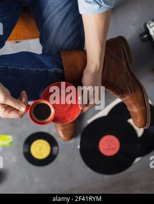 Männliche Hand hält Tasse Kaffee und Bein in Jeans mit alten Reisen Lederstiefel Schuhe. Mann und entspannen Lebensstil Konzept Stockfoto