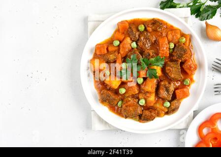 Rindereintopf mit Kartoffeln und Karotten in Tomatensauce auf weißem Steinhintergrund mit Kopierraum. Draufsicht, flach liegend Stockfoto