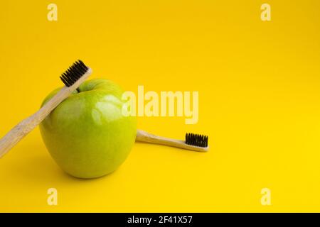 Zwei Bambuszahnbürsten und grüner Apfel auf dem gelben Hintergrund.Platz kopieren. Stockfoto