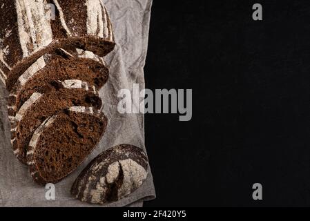 Geschnittenes Roggenbrot auf schwarzem Hintergrund. Rustikales handwerkliches Brot. Speicherplatz kopieren Stockfoto