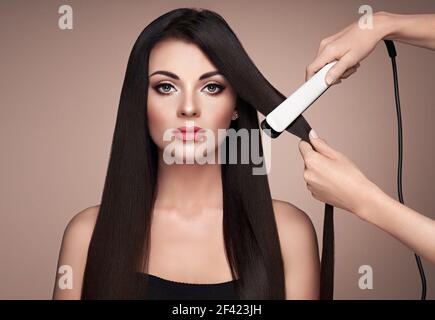 Friseur glätten lange dunkle Haare mit Fön Bügeleisen. Schöne Frau mit langen, glatten Haaren. Glatte Frisur Stockfoto
