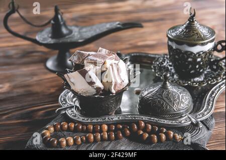 Eine Schüssel mit verschiedenen Stücken türkischer Sonnenblumenhalva und schwarzem Tee auf einem hölzernen Hintergrund. Das Konzept einer festlichen orientalischen Tee-Party. Stockfoto