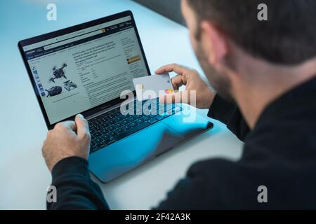 London, England, 12. März 2021. Blick von hinten auf einen Mann, der zu Hause auf Amazon auf seinem Laptop schaut und einkauft Stockfoto