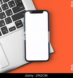 Business-Modell mit Mobiltelefon mit leerem weißen Bildschirm, Laptop im Hintergrund Stockfoto
