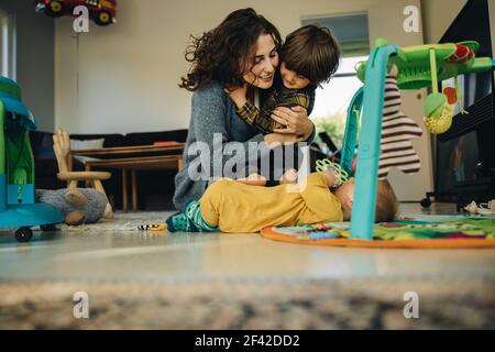 Mutter mit ihren beiden Kindern zu Hause. Frau im Mutterschaftsurlaub Spaß mit ihren Kindern im Haus. Stockfoto