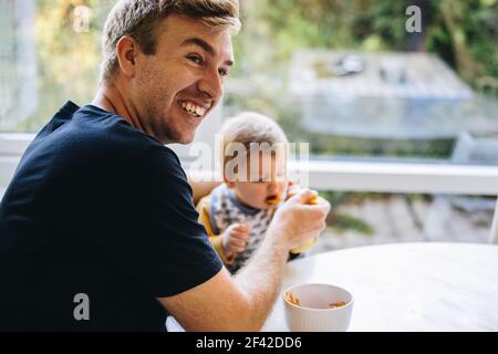 Lächelnder Mann Fütterung Baby mit Löffel, Vater kümmert sich um sein Baby, während in Vaterschaft verlassen. Stockfoto