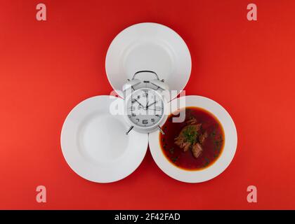 Intermittierendes Fastenkonzept. Leerer weißer Teller, Wecker und Suppe. Gesundes Lebensmittelkonzept. Gewichtsverlust. Stockfoto