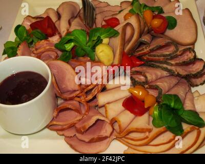 Vorspeise aus verschiedenen Fleischprodukten, garniert mit Kirschtomaten und Kräutern. Geräucherter und gekochter Schinken Stockfoto