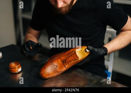 Nahaufnahme eines nicht erkennbaren Schusters in schwarzen Handschuhen, die Farbe auf hellbraunen Lederschuhen mit den Fingern reiben. Stockfoto