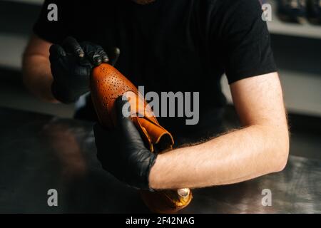 Nahaufnahme des Schusters in schwarzen Handschuhen, die Farbe auf der Zehenspitze der braunen Lederschuhe mit den Fingern reiben. Stockfoto