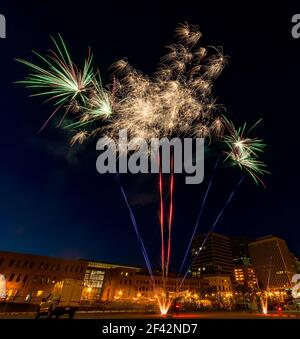 Feuerwerk. Weitwinkel-Aufnahme zeigt den Start sowie die Blüten. Gebäude und Straßenbeleuchtung im Hintergrund. Der Fokus liegt auf dem Feuerwerk. Stockfoto