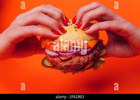 Die Hälfte der Brötchen mit Sesamsamen auf einem großen saftigen Burger geben. Burger mit Käse, Gemüse und zwei Schnitzel. Roter Hintergrund Stockfoto