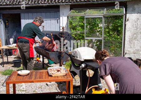 Mann und Frau braten ganze Schweine und Würstchen auf Außengrill. Stockfoto