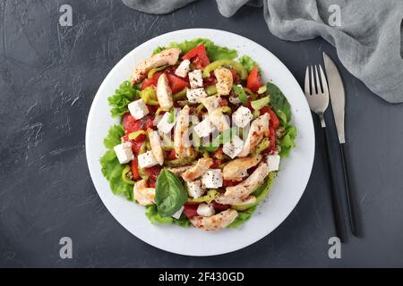 Salat mit Bulgur, gebackenem Huhn, Paprika, Basilikum und Feta auf einem weißen Teller auf grauem Hintergrund. Blick von oben Stockfoto