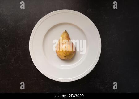 Gelbe Birne auf Runde weiße Platte gegen schwarzen Hintergrund Stockfoto