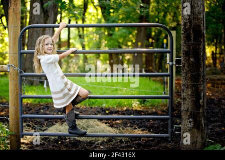 Kleines blondes Mädchen klettert ein Tor auf der Farm. Stockfoto