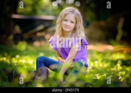 Schöne kleine blonde Mädchen in lila Hemd auf dem Gras sitzen. Stockfoto