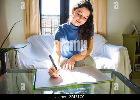 Junge Frau, die im Wohnzimmer studiert und schreibt Stockfoto