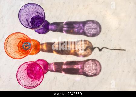 Drei bunte Kindertrinkbecher und lange Schatten auf einem strukturierten grauen und weißen Marmorhintergrund mit einer modernen Draufsicht. Stockfoto