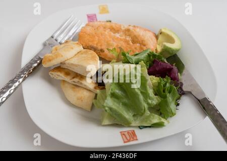 Lachssalat mit Avacado, grünen Blättern und gerösteten Broten auf weißem Hintergrund Stockfoto