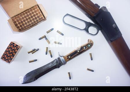 Jagdkonzept mit einem Hebelgewehr, einem mit Knochen gehandhabten Jagdmesser und .22 Kaliber Geschosse verstreut und in einer Box auf weißem Hintergrund. Stockfoto