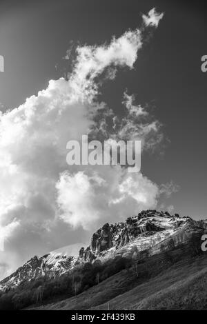 Eine Graustufenaufnahme von felsigen Bergen, die teilweise von Schnee bedeckt sind Auf dem Hintergrund des bewölkten Himmels Stockfoto