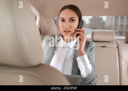 Besorgte Geschäftsfrau, die auf dem Rücksitz des Autos telefoniert Stockfoto