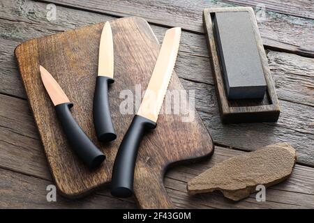 Tafel mit Messern und Schleifstein auf Holz Hintergrund Stockfoto