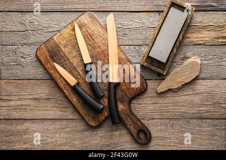 Tafel mit Messern und Schleifstein auf Holz Hintergrund Stockfoto