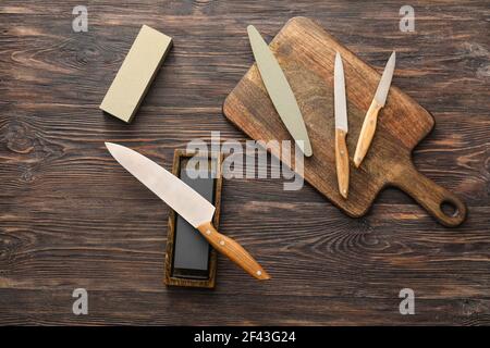Tafel mit Messern und Schleifstein auf Holz Hintergrund Stockfoto