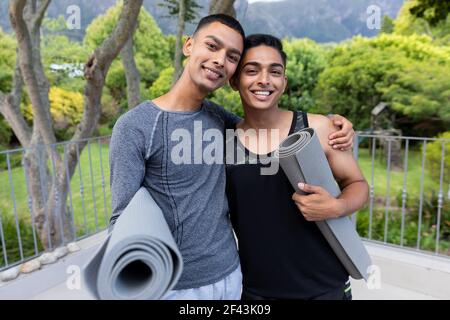 Portrait von verschiedenen Homosexuell männlichen Paar hält Yoga-Matten und Lächelnd auf dem Balkon Stockfoto