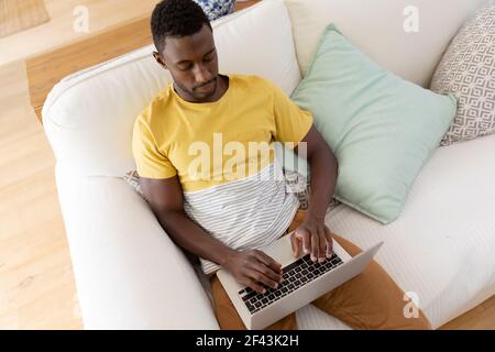 afroamerikanischer Mann, der mit einem Laptop auf dem Sofa sitzt Stockfoto