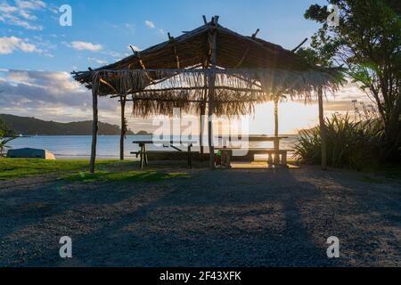 Strohdach Schutz am Mulberry Grove Beach Silhouette gegen goldenen Sonnenuntergang auf Great Barrier, Stockfoto