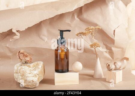 Braune Glasflasche mit Pumpe von Kosmetikprodukten auf Stein, geometrische Holzformen und getrocknete Blumen auf beigem Papierhintergrund. Natürliches organisches Spa C Stockfoto