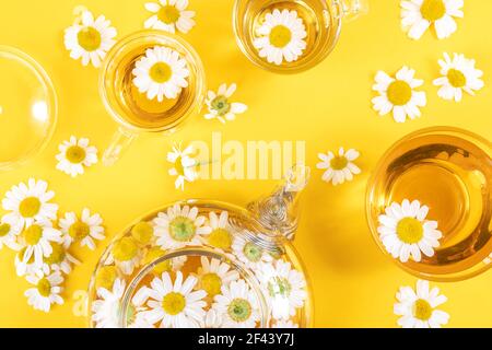 Drei Tassen Tee und transparente Teekanne mit Kamillenblüten auf gelbem Hintergrund. Kamille Tee Vorteile Ihr Gesundheitskonzept. Draufsicht Flat Lay. Stockfoto