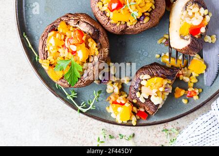 Gebackene gefüllte portobello-Pilze mit Bulgur-Pilaf und gehacktem Gemüse. Leckeres und nahrhaftes vegetarisches Gericht. Steinhintergrund, selektiver FOC Stockfoto