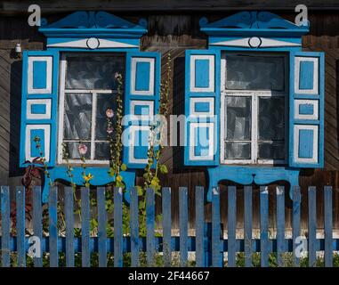 Russische alte braune Blockhütte mit weißen und blauen Fensterläden in Tinskoy, Russland. Stockfoto