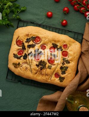 Focaccia, Fladenbrot mit Tomaten, auf dunkelgrünem Leinentischtuch. Draufsicht Stockfoto