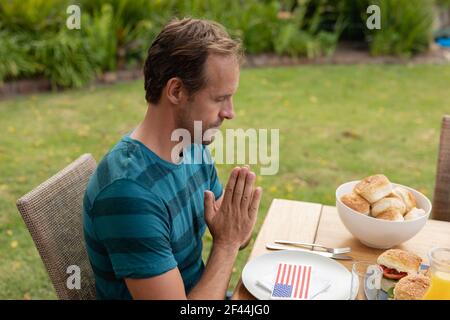 Kaukasischer Mann mit Händen im Gebet sagen Gnade vor dem Essen Essen mit der Familie im Garten Stockfoto