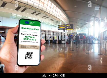 Der digitale grüne Pass der europäischen Union mit dem QR-Code auf dem Bildschirm eines Handys an einer Hand gehalten mit verschwommenem Flughafen im Hintergrund. Immunit Stockfoto