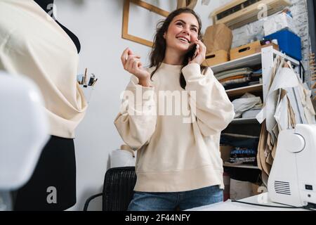 Lächelnd schön Brünette Mädchen Näherin im Gespräch auf Handy, während Arbeiten im Atelier Stockfoto