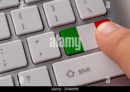 Männliche Hand drücken Tastatur-Taste mit Flagge von Italien auf sie. Online internationales Geschäftskonzept. Stockfoto