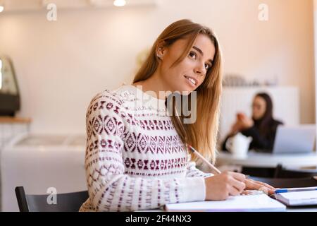 Zufrieden charmante Student Mädchen tun Hausaufgaben, während im Café sitzen In Innenräumen Stockfoto