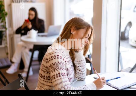 Lächelnd charmante Student Mädchen Hausaufgaben machen, während im Café sitzen In Innenräumen Stockfoto