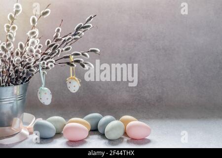 Ostern minimalistischer Hintergrund mit Weidenkattenzweigen in einem dekorativen Eimer und farbenfrohe Ostereier mit Platz zum Kopieren Stockfoto