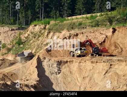 Bagger beladen den Sand auf den schweren Bergbauwagen im Tagebau. Schwere Maschinen arbeiten im Bergbau Steinbruch. Graben und Aushubarbeiten. Stockfoto