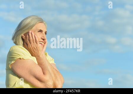 Gerne ältere Frau gegen den blauen Himmel posing Stockfoto